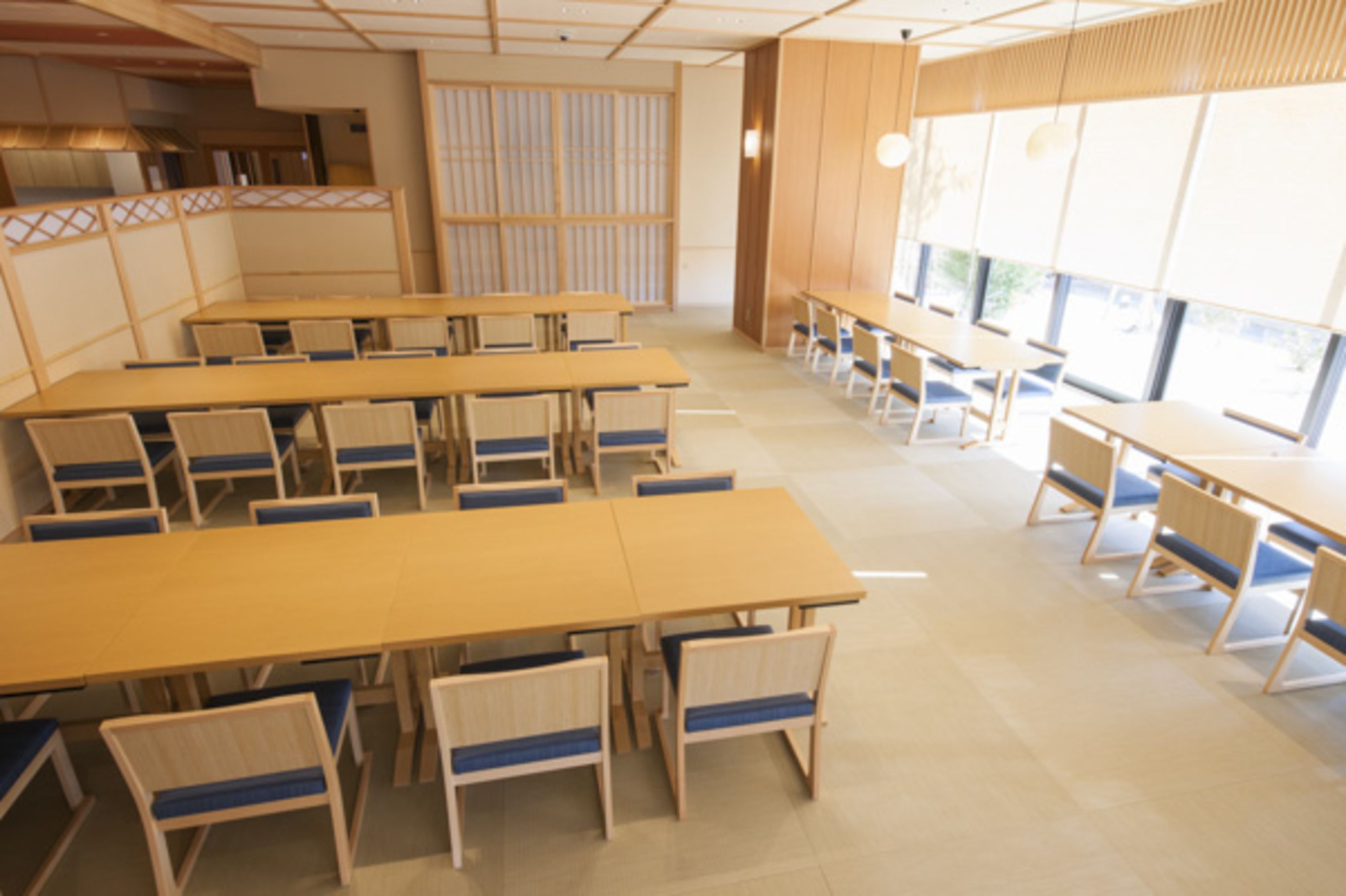 A spacious room with multiple tables and chairs, large windows, and a traditional Japanese sliding door.
