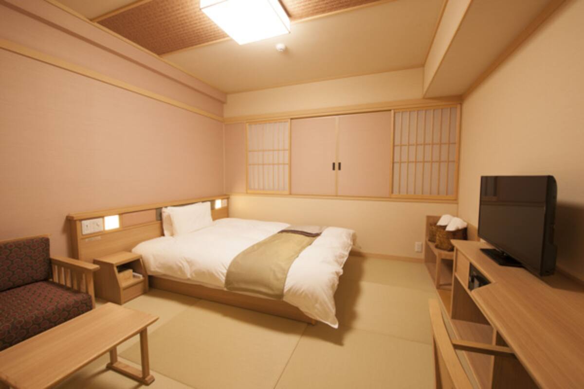 A hotel room with a bed, a TV, a desk, and a sofa.