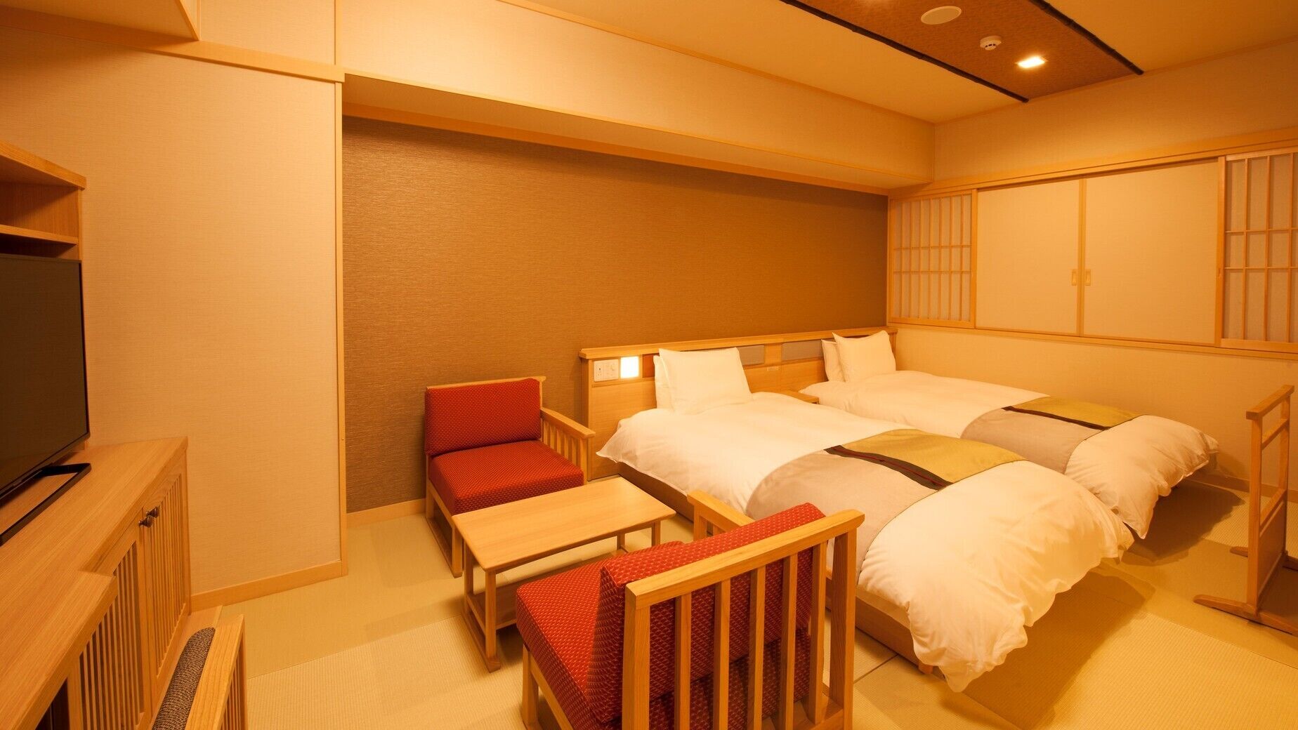 A hotel room with two beds, a TV, a small table, and a chair.