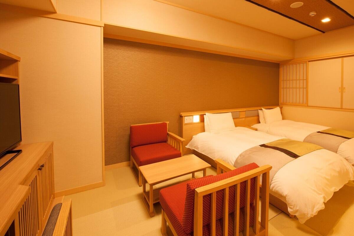 A hotel room with two beds, a TV, a small table, and a chair.