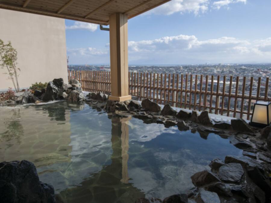 Een traditioneel Japans onsen met een houten hek en uitzicht op de stad.