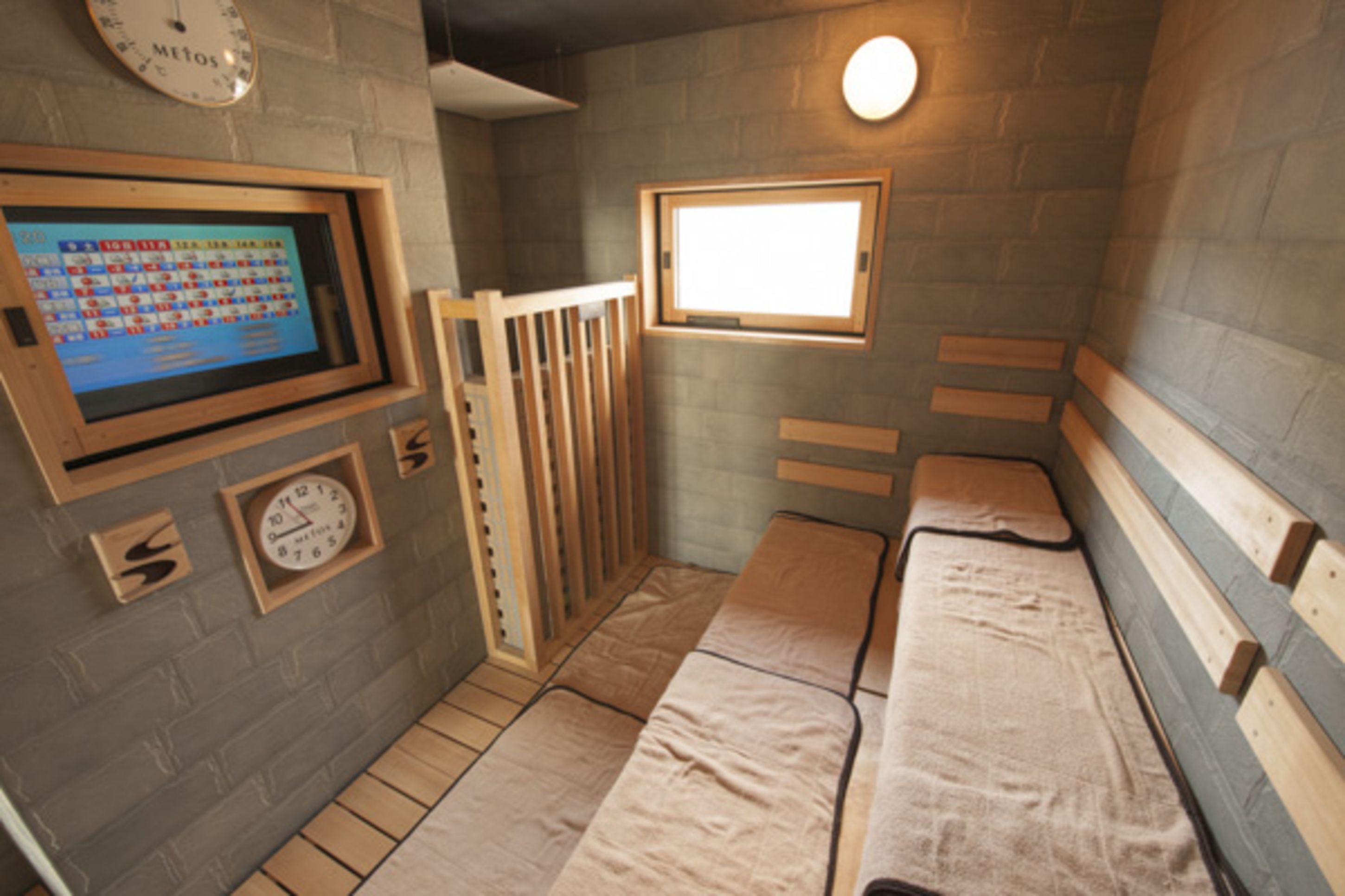 A small, enclosed room with a wooden bench, a window, a clock, and a digital display on the wall.