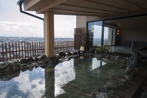 A hot spring area with a wooden fence, rocks, and a view of the cityscape. - Onyado Nono Sakaiminato Natural Hot Spring (Sakaiminato)