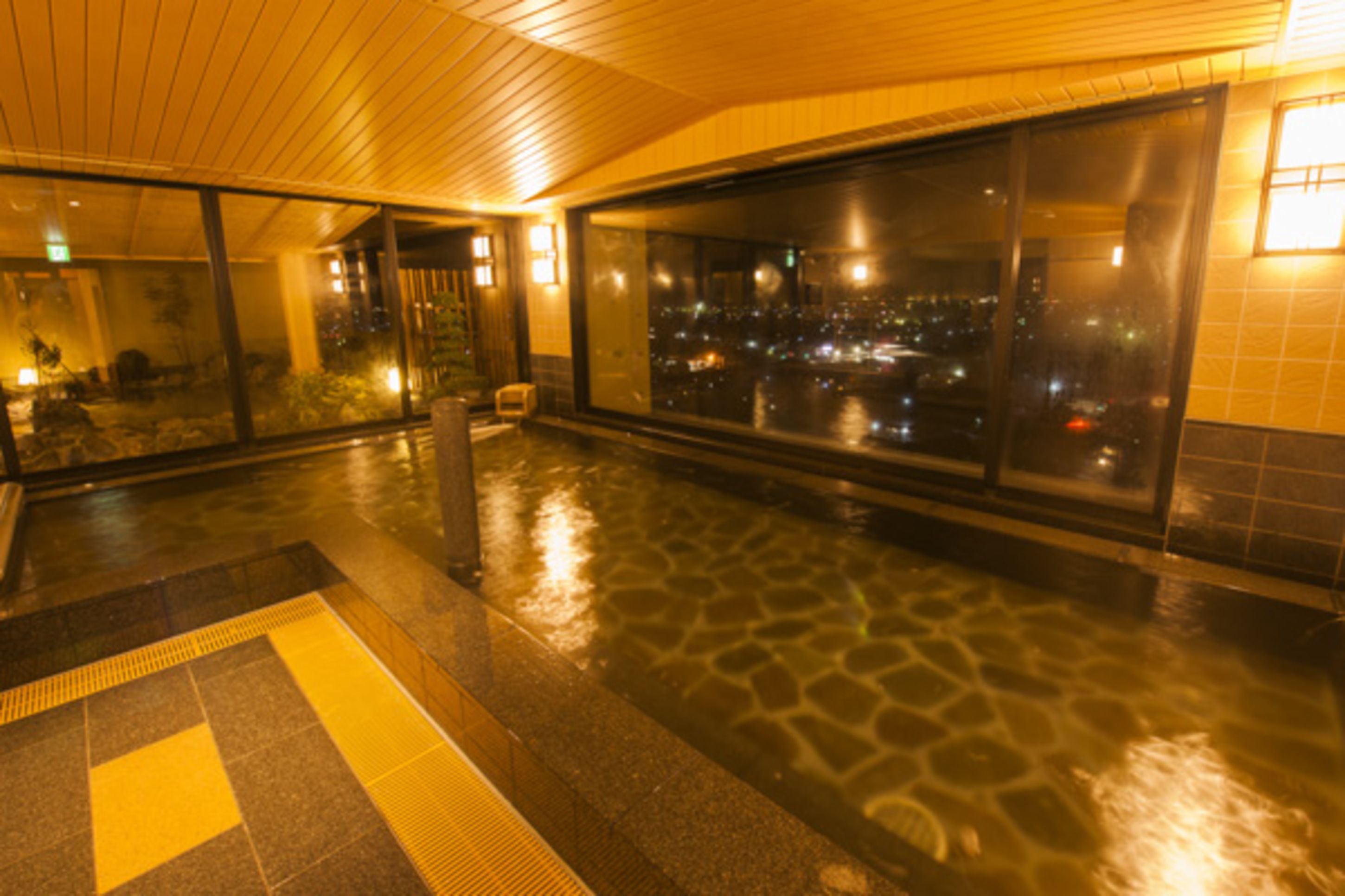 A wet stone floor with a yellow tactile path leading to a glass door.