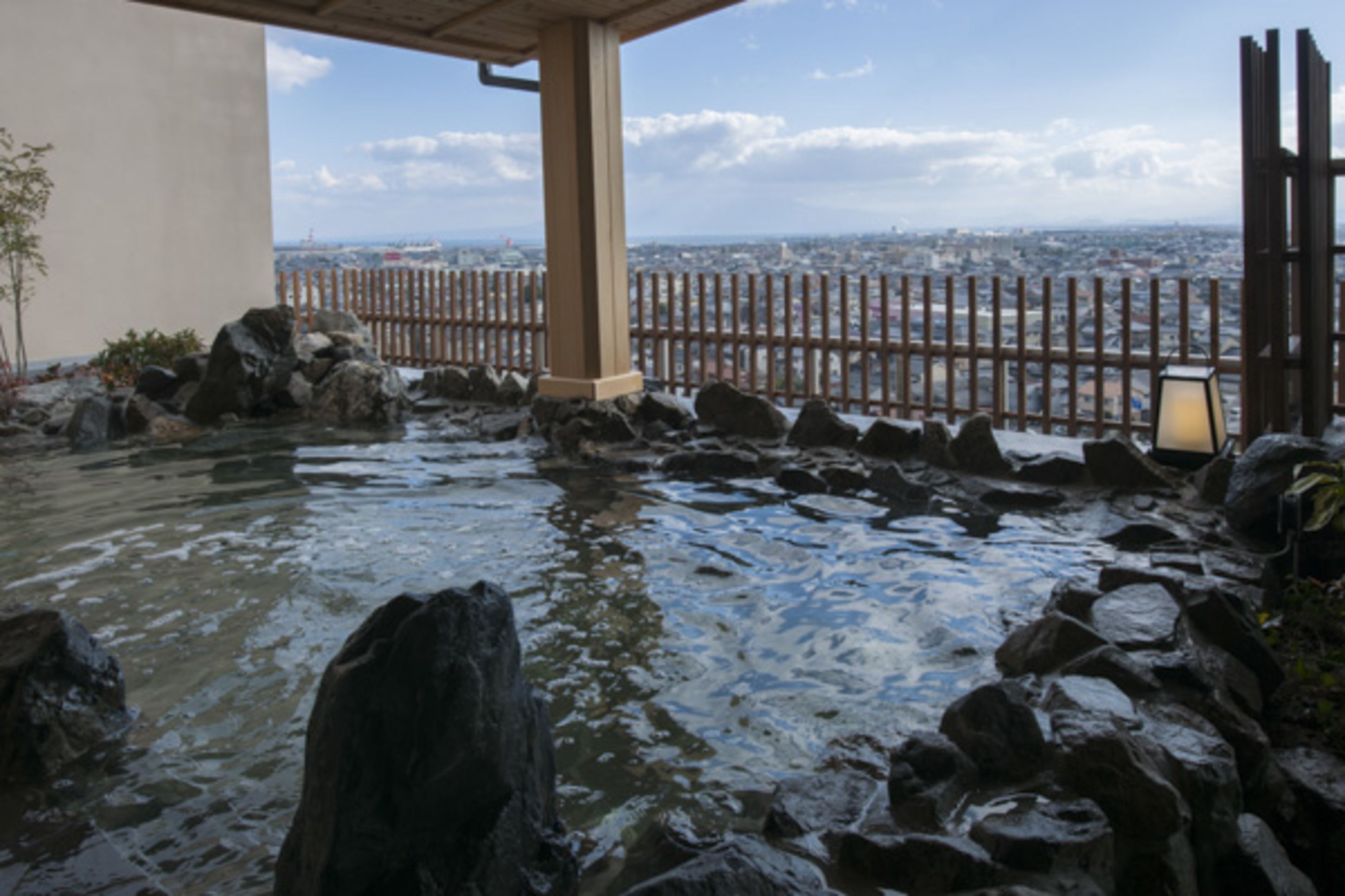 Un élément décoratif aquatique composé de rochers, agrémenté d’une clôture en bois et offrant une vue sur le paysage urbain.