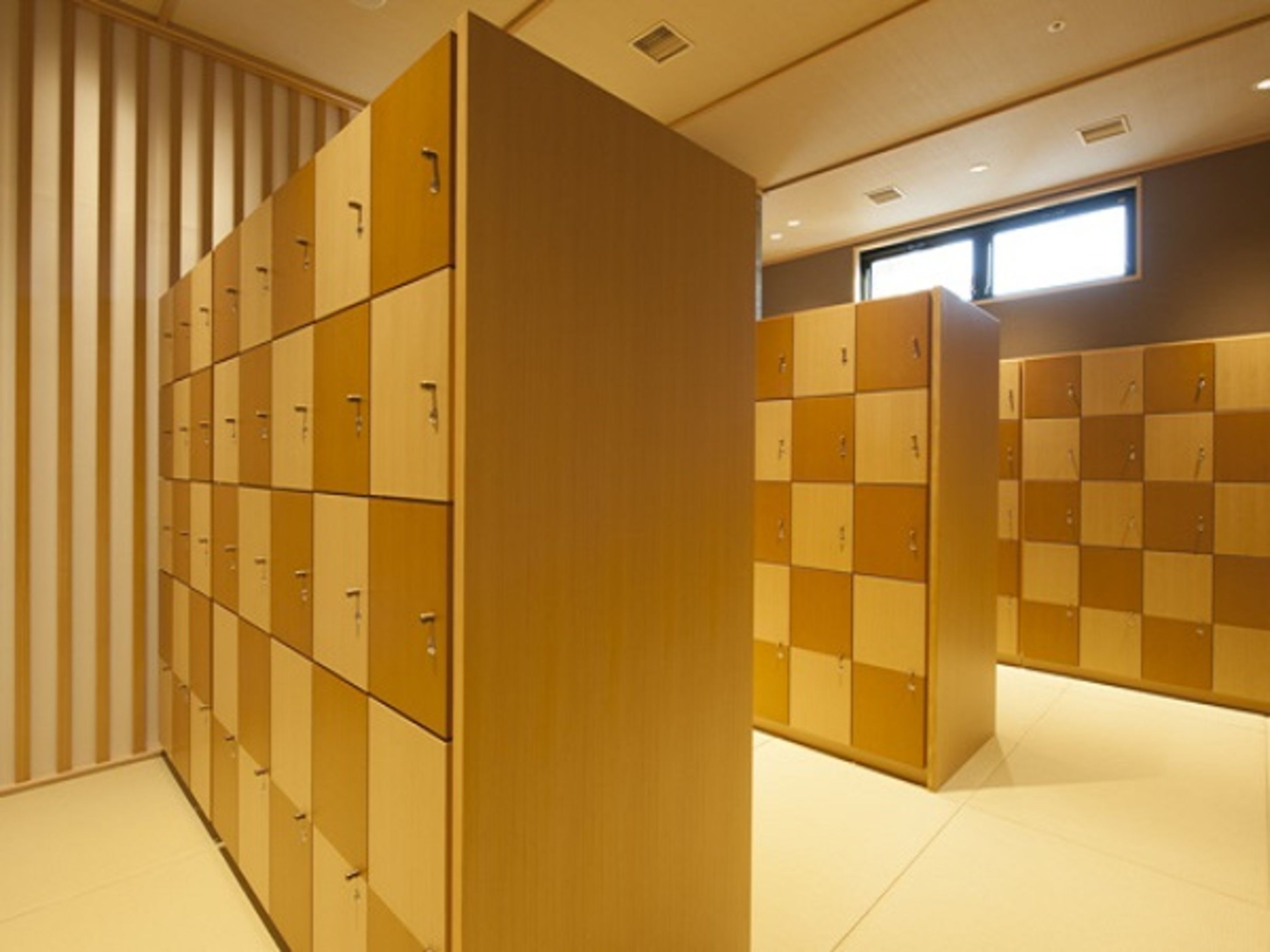 A row of lockers with a checkered pattern, a wooden panel wall, and a window providing natural light.