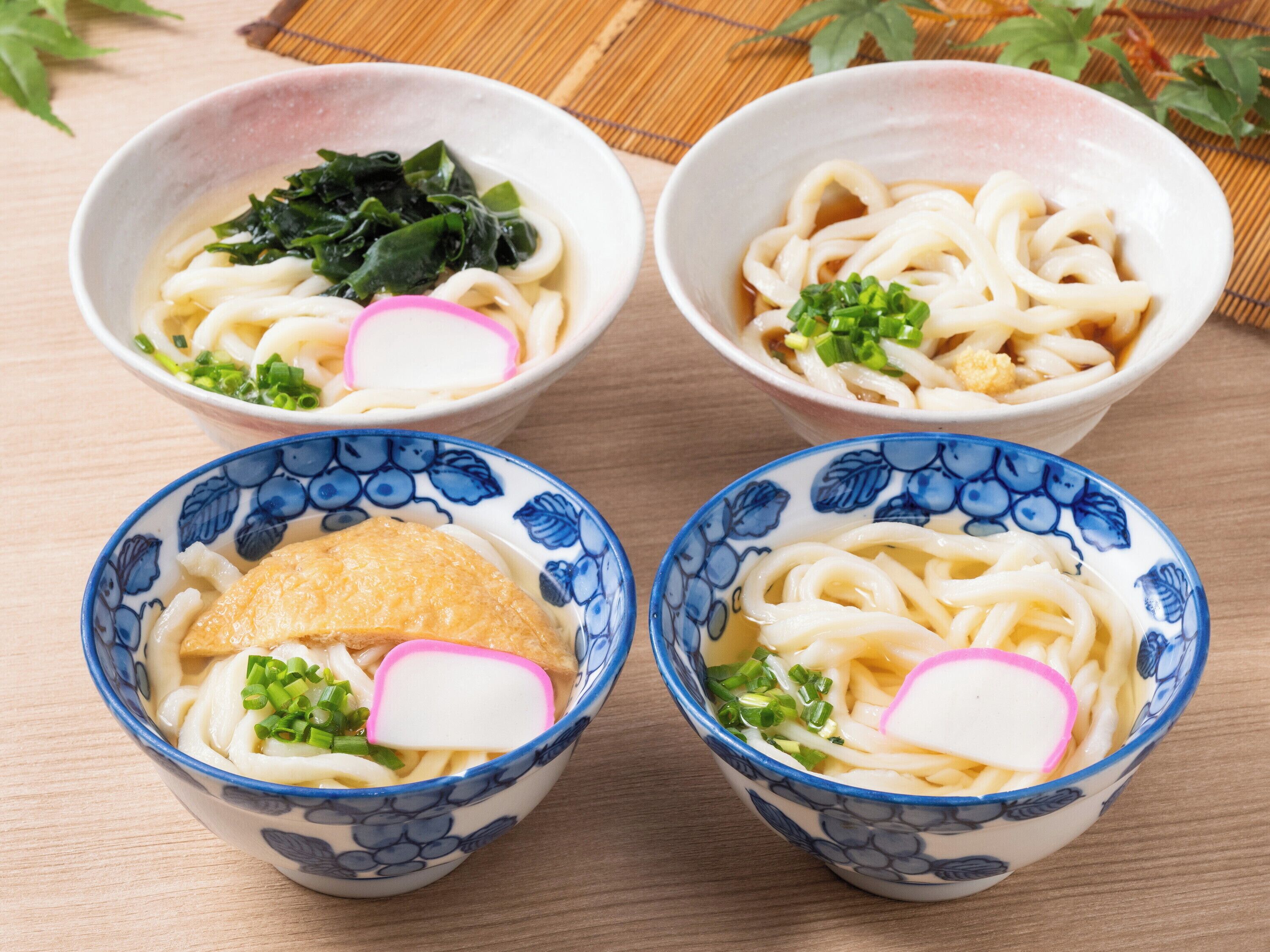 Four bowls of ramen with toppings, placed on a wooden table.