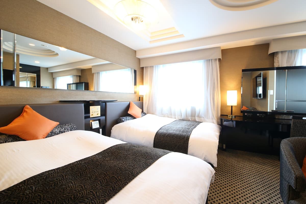 A hotel room with two beds, a desk, a chair, a TV, and a large mirror.