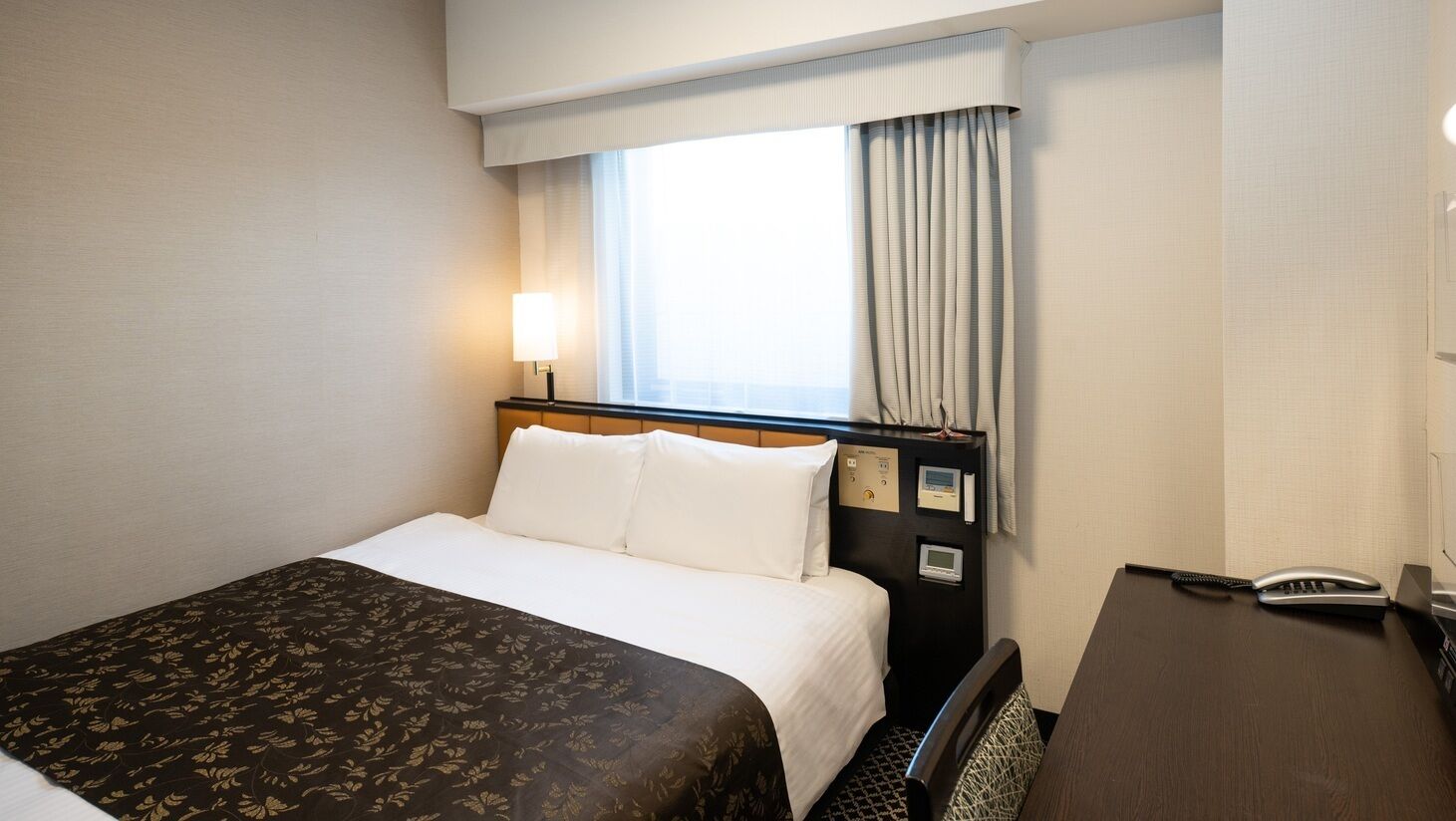 Een hotelkamer met een bed, nachtkastje, lamp en raam met gordijnen.