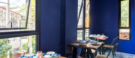A dining area with blue walls, large windows, and wooden tables set with bowls and glasses.