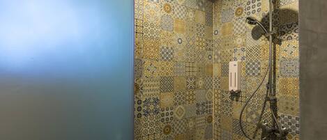 A shower with a patterned tile wall and a handheld showerhead.
