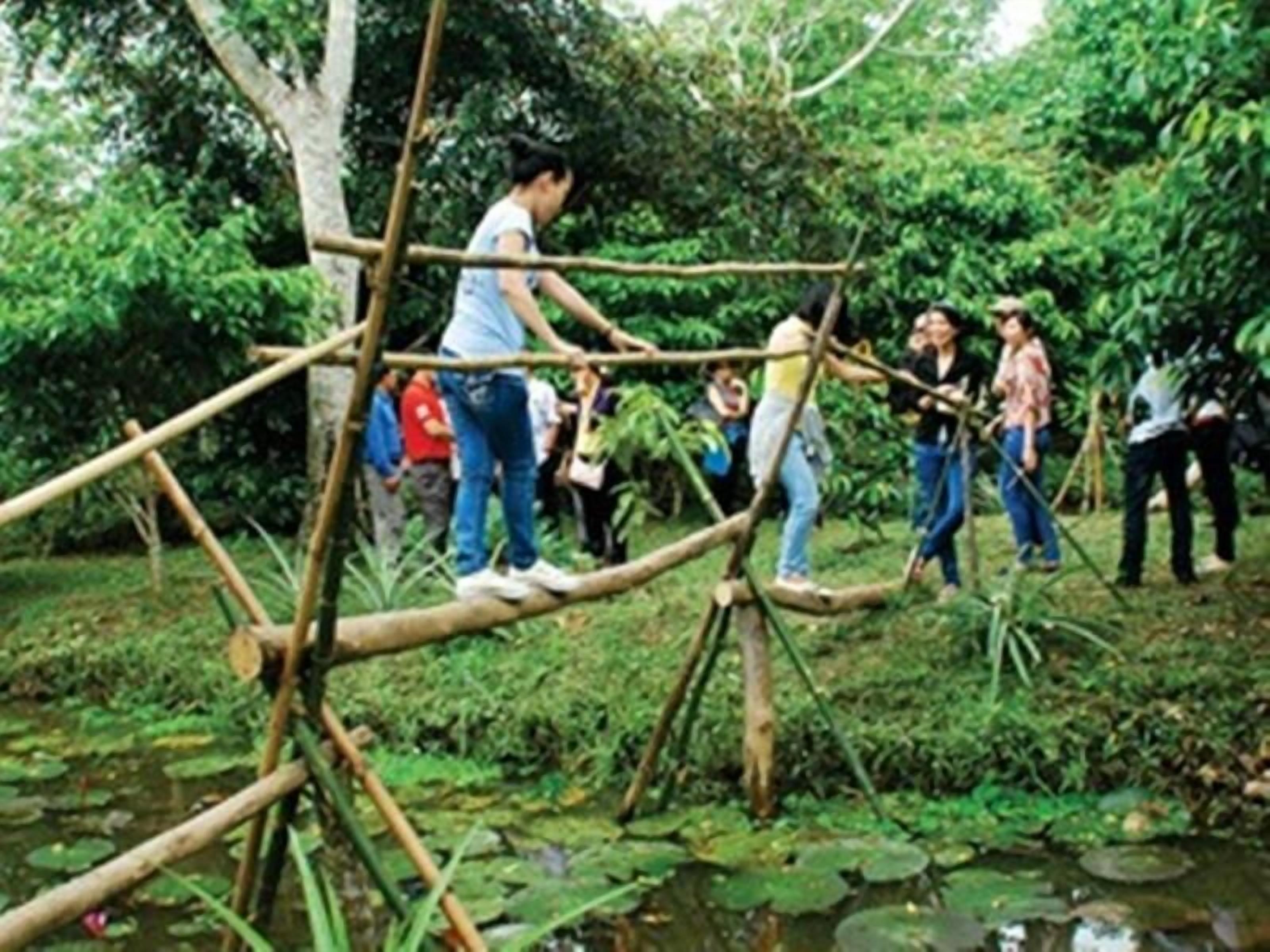 A group of people crossing a bamboo bridge over a pond surrounded by lush greenery.