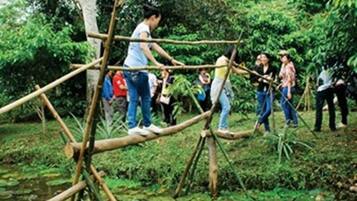 A group of people crossing a bamboo bridge over a pond surrounded by lush greenery.