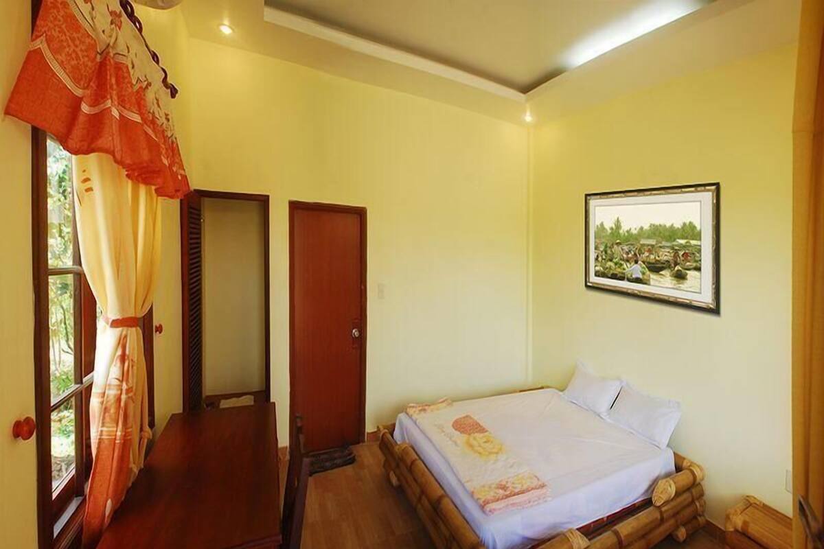 Una habitació amb un llit, una taula de treball, una porta i una finestra amb cortines.