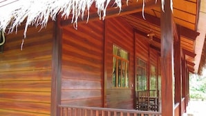 Una cabaña de madera con porche, cimientos de piedra y techo de paja.