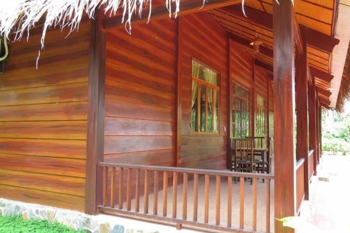 Una cabana de fusta amb un porxo, fonaments de pedra i un teulat de palla.