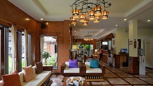 A spacious lobby with a brick wall, a seating area with cushions, a chandelier, and a reception desk.