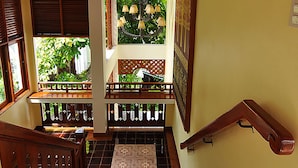 A wooden staircase with a handrail, a tiled floor, and a view of greenery outside.