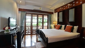 A hotel room with a bed, a desk with a computer, a window with curtains, and a door leading to a balcony.