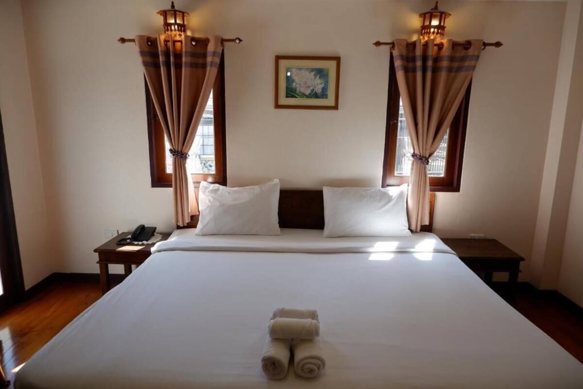 Une chambre d’hôtel avec un grand lit, deux tables de chevet, une petite table et un tableau encadré au mur.