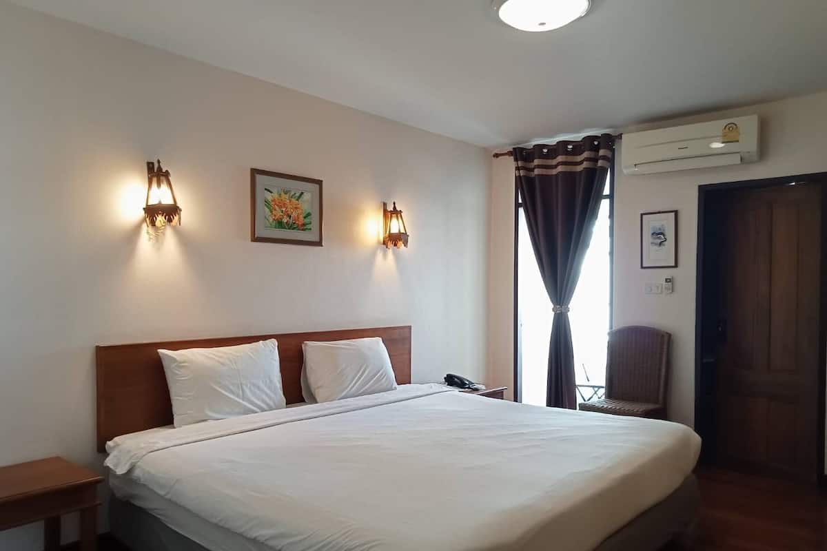 Une chambre d’hôtel avec un grand lit, deux lampes fixées au mur, un climatiseur, une chaise et une fenêtre avec des rideaux.
