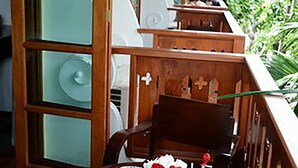 A wooden outdoor seating area with a table set for two, featuring a menu, a drink, and a vase with flowers.