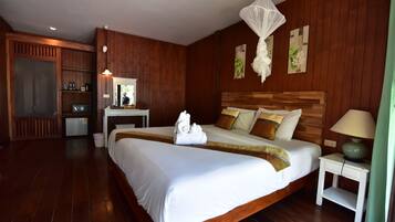 A hotel room with a large bed, wooden walls, a bedside table with a lamp, and a small desk with a mirror and coffee machine.
