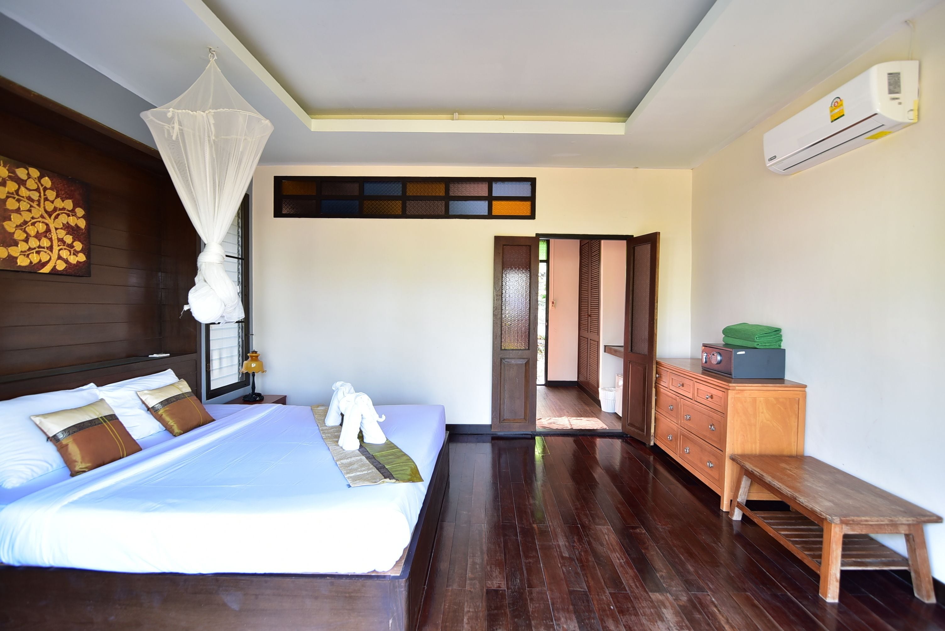 Une chambre d’hôtel comprenant un lit, une table de chevet, une lampe, un appareil de climatisation, un banc en bois et une vue sur l’extérieur.
