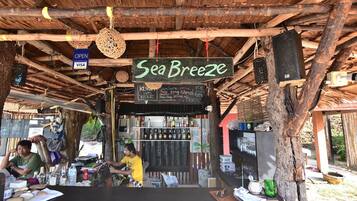 A rustic outdoor bar with a thatched roof, wooden beams, and a sign reading "Sea Breeze".