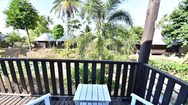A wooden deck with a table and two chairs, overlooking a tropical landscape with palm trees and a small building. - Koh Ngai Thanya Beach Resort (Ko Lanta)