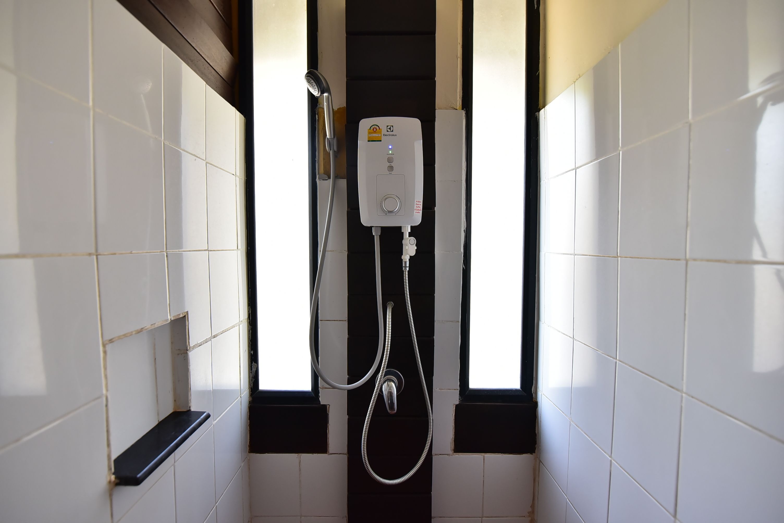 A bathroom with white tiled walls, a black bathtub, and a shower unit with a control panel.