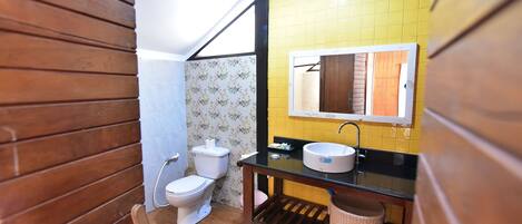 A bathroom with a wooden floor, a white toilet, a sink with a mirror above it, and a yellow tiled wall.