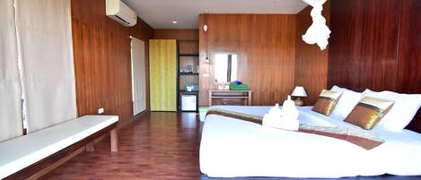 A hotel room with a wooden floor, a bed with white bedding, a bench, a desk with a chair, and a window.