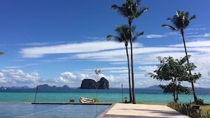 A poolside view with palm trees, a lounge chair, and a view of the ocean and distant islands.