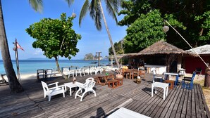 A wooden deck with white and blue outdoor furniture, a thatched-roof structure, and a view of the ocean.