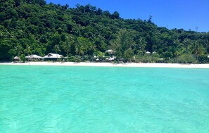 A beach with clear turquoise water, a sandy shore, and a forested hill in the background. - Koh Ngai Thanya Beach Resort (Ko Lanta)