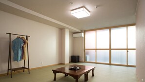 A room with tatami flooring, a wooden table with a tray, a clothing rack, and a sliding glass door with a view. - Seibido Inn - Hostel (Kyoto)