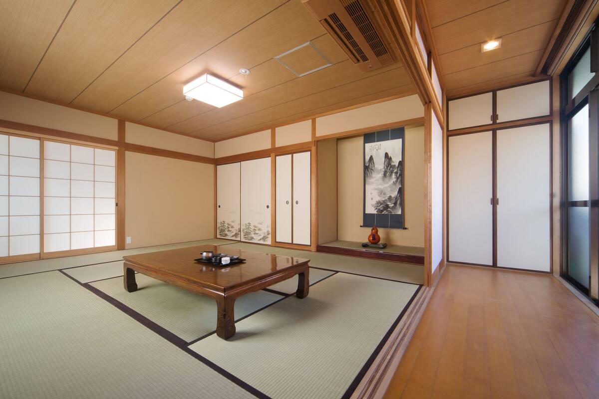 A traditional Japanese room with tatami flooring, a low wooden table, sliding doors, and a large window.