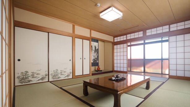 A traditional Japanese room with tatami flooring, a low wooden table, sliding shoji doors, and a view through large windows. - Seibido Inn - Hostel (Kyoto)