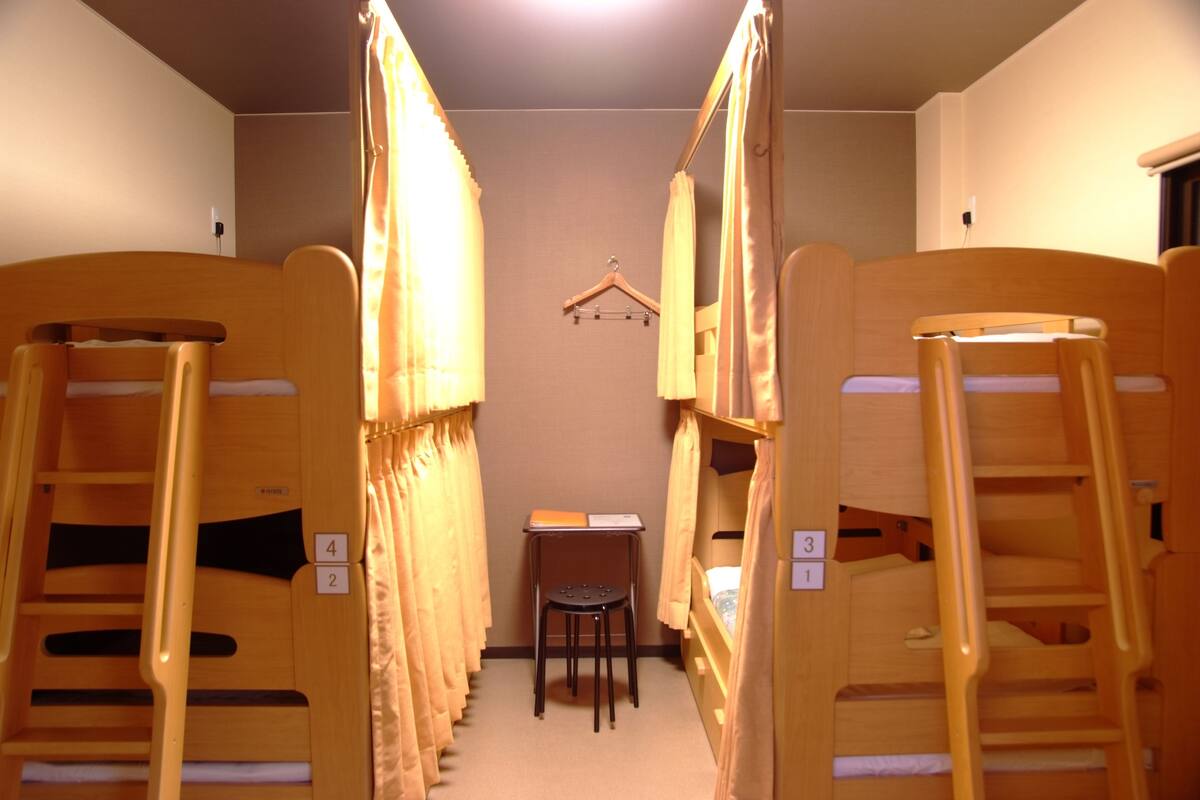 A narrow room with bunk beds, a small table, and a chair.