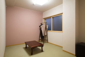A room with a wooden bench, a clothes rack with patterned items, a window with blinds, and a light fixture on the ceiling. - Seibido Inn - Hostel (Kyoto)