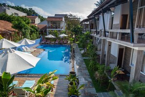 A pool area with lounge chairs and umbrellas, surrounded by greenery and buildings.