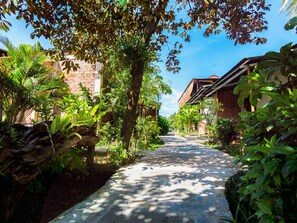 A pathway flanked by lush greenery and traditional architecture, leading to a building with a sloped roof. - Lan Anh Garden Resort (Phu Quoc)