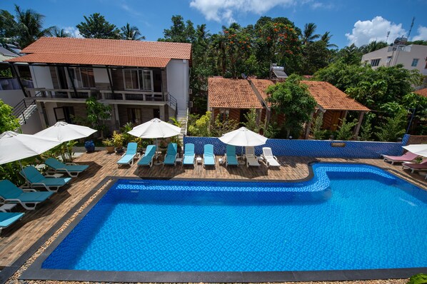 A swimming pool with lounge chairs and umbrellas, surrounded by buildings with red-tiled roofs.