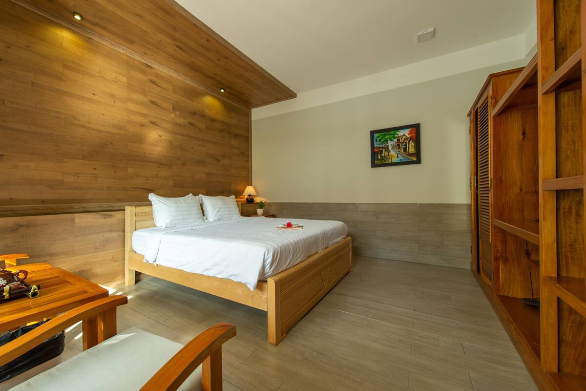 Ein Schlafzimmer mit einem hölzernen Bett, einem Nachttisch, einer Lampe, einer Holzbank und einem Holzschrank.