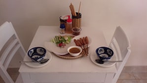 A dining table with a white tablecloth, two blue and white patterned bowls, a plate with food, a small bowl of sauce, and a basket with utensils.
