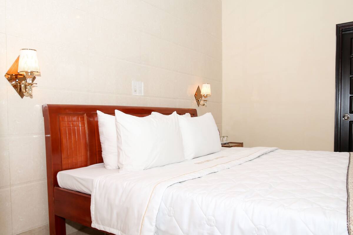 A neatly made bed with white linens and a wooden headboard in a hotel room.