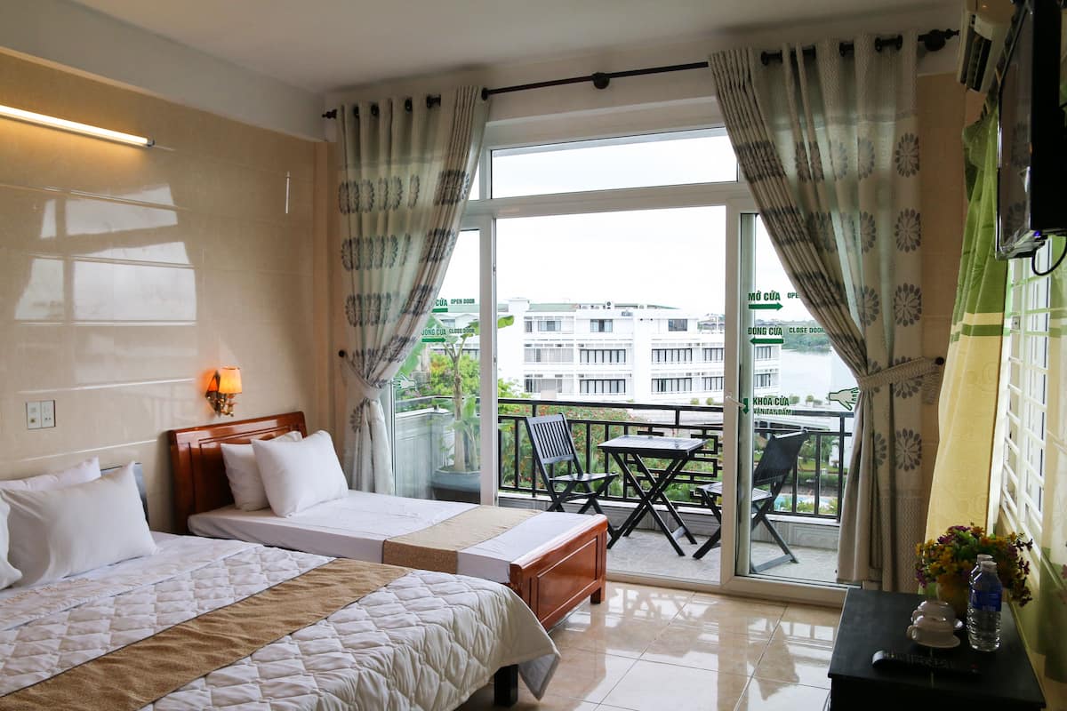 A hotel room with two beds, a balcony with a table and chairs, and a view of the city.