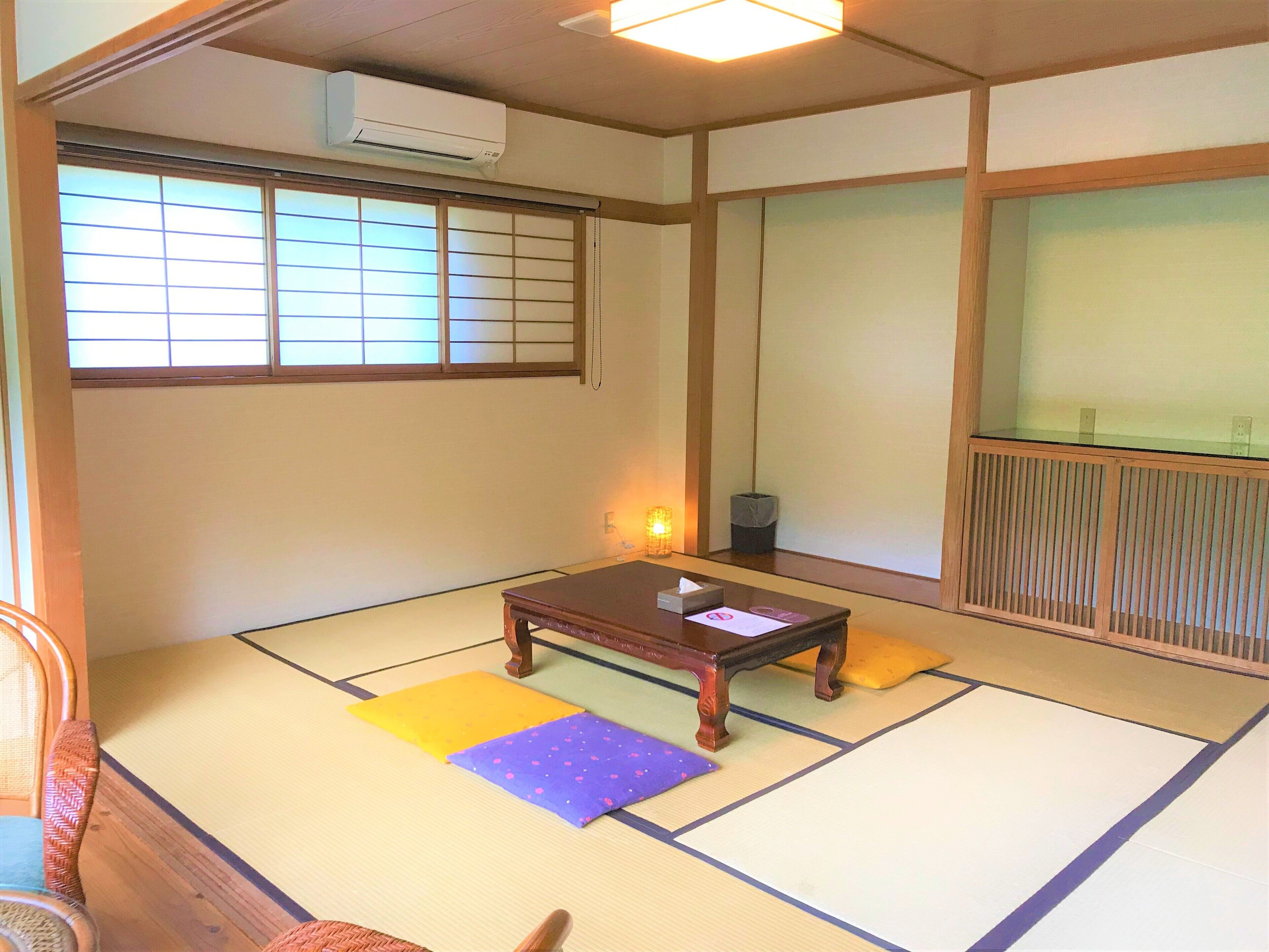 A traditional Japanese room with tatami flooring, a low wooden table, a cushion, and a sliding door.