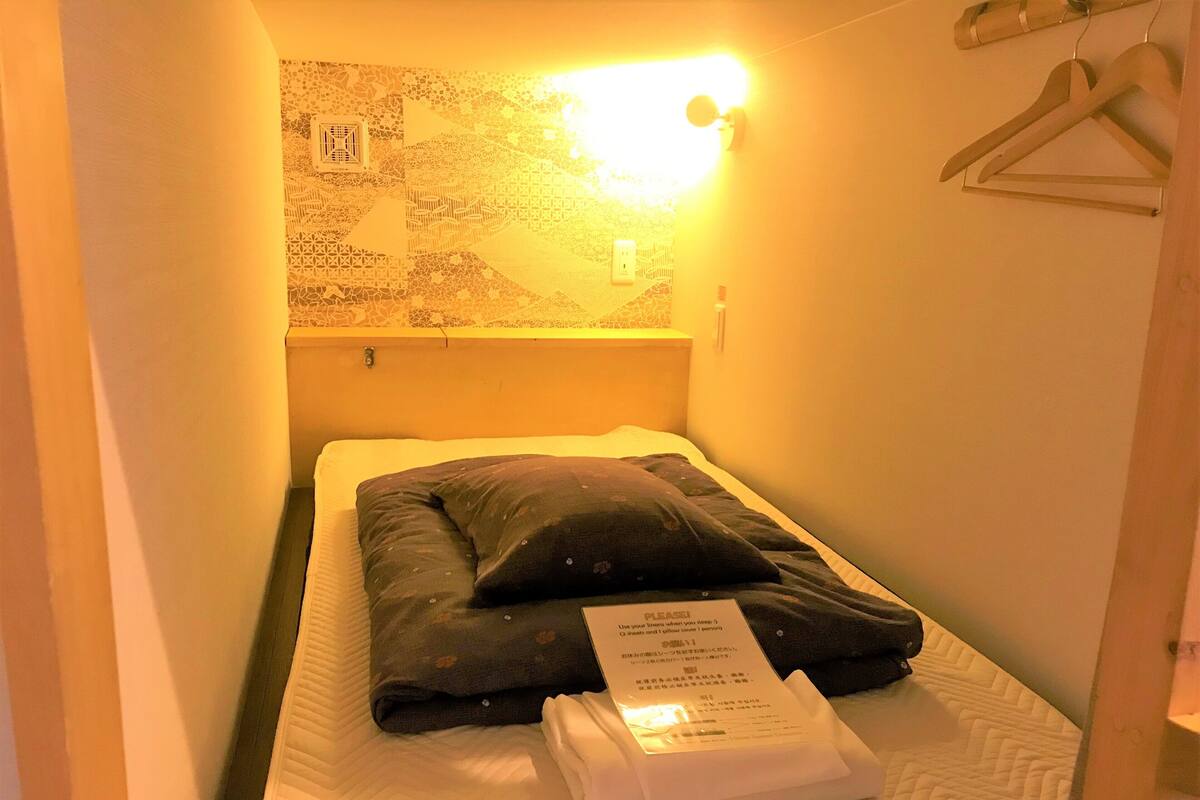 Una habitación pequeña con una cama individual, pared con diseño, lámpara de noche y perchero.